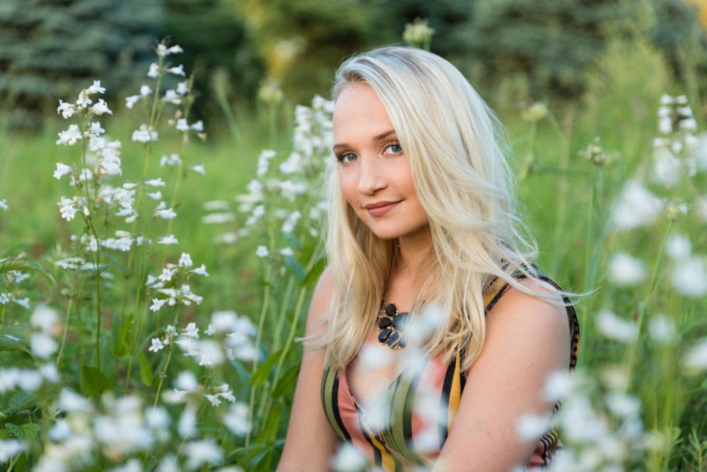 Blonde high school senior sitting in long wild flowers