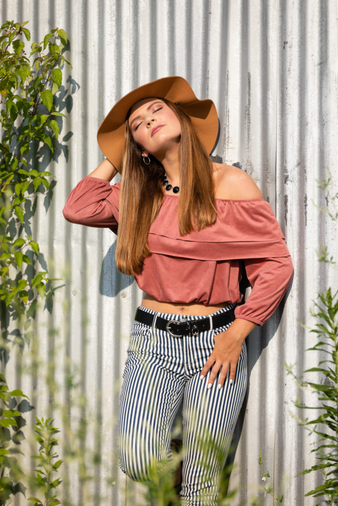 Senior Graduate poses outdoors against a tin shed