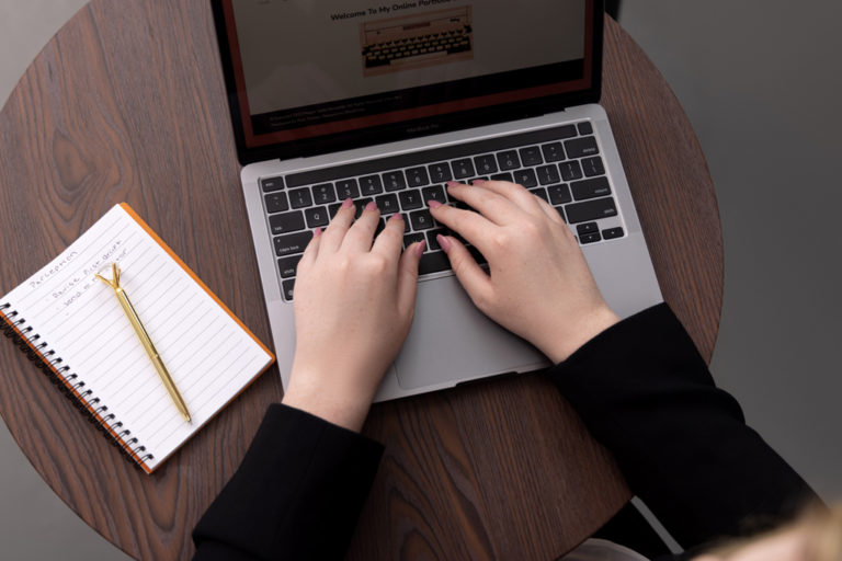 Personal Branding Sessions for women. Woman sitting at computer with notebook and pen showing a close up of her hands.