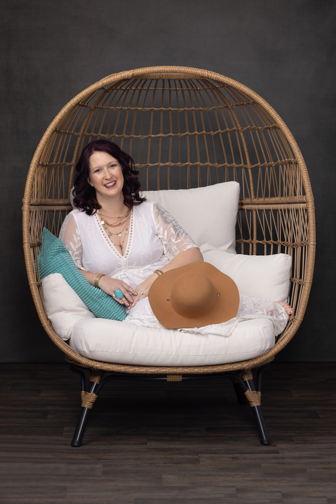 Bloomington IL Photographer to empower woman. Woman is sitting in an egg chair with a floppy hat and turquoise pillow.