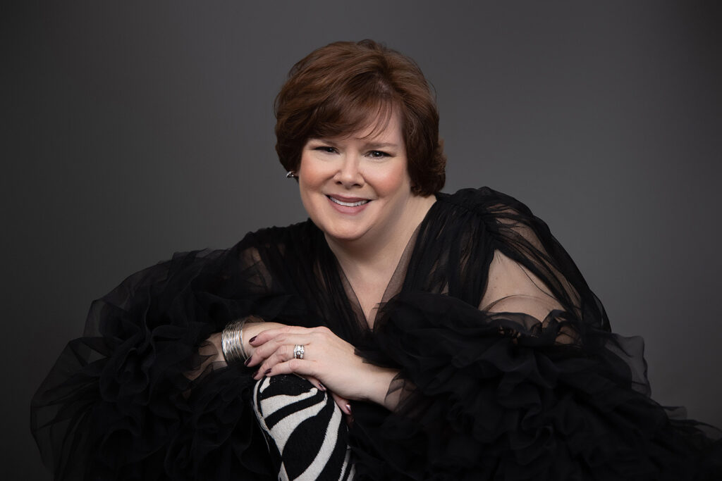 bloomington glamour photographer. This mature woman is wearing a black tool gown accented with silver jewelry sitting on a zebra pattern chair