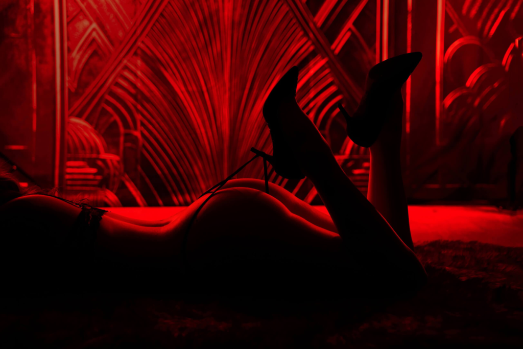 Silhouetted woman lying on stomach in red light with heels raised.