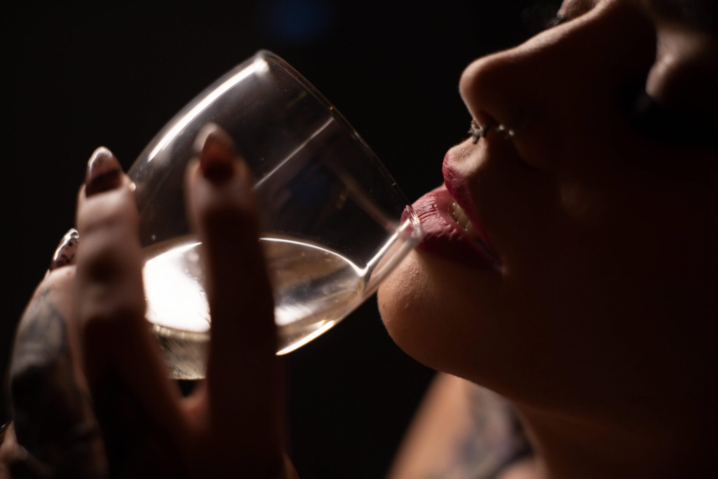 Tattooed woman in black lace bodysuit posing on stool with red studio lights.