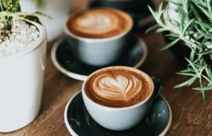 Two cups of latte art coffee on a wooden table with plants nearby. — bloomington il coffee shops